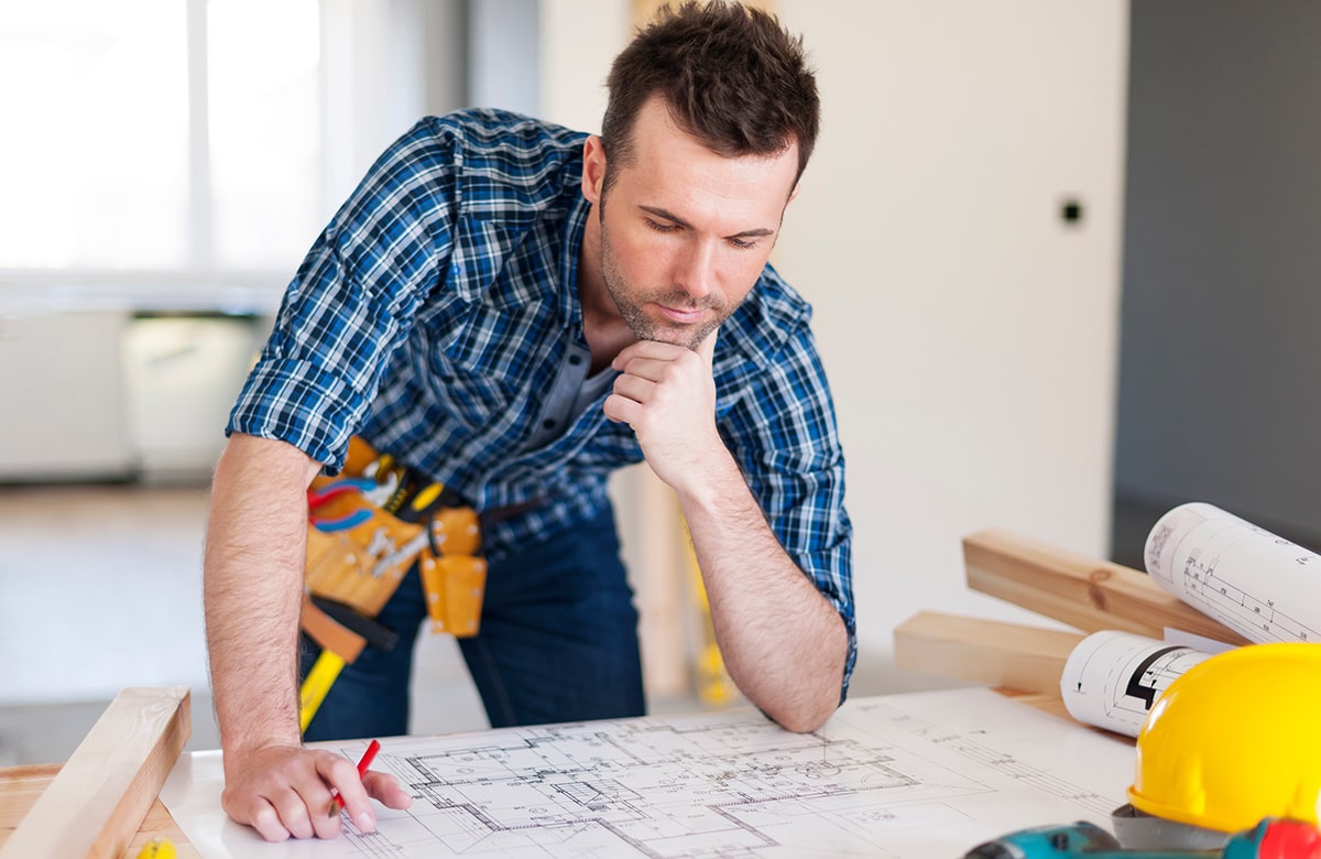 A man intently studies a blueprint while overseeing a construction site.